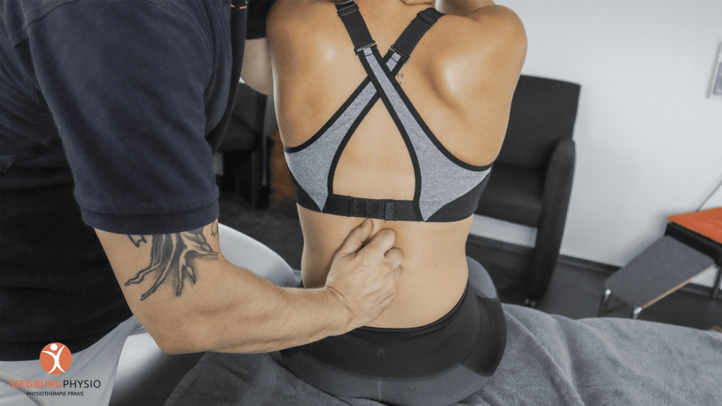 Therapeut behandelt unteren Rücken einer Frau in Sportkleidung auf einer Behandlungsliege