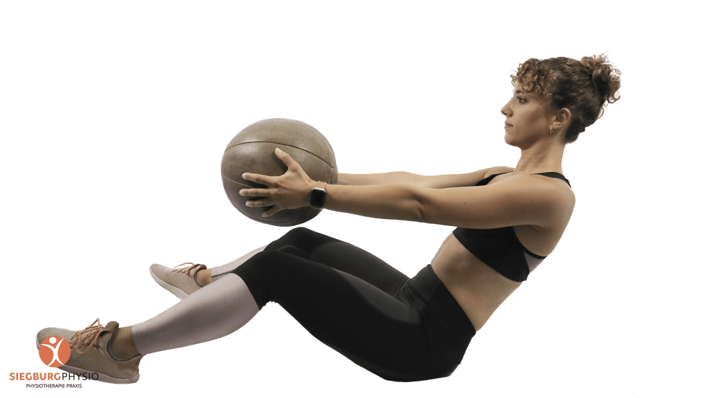 Junge Frau in Trainingskleidung führt eine Übung mit einem Medizinball aus zur Krankengymnastik