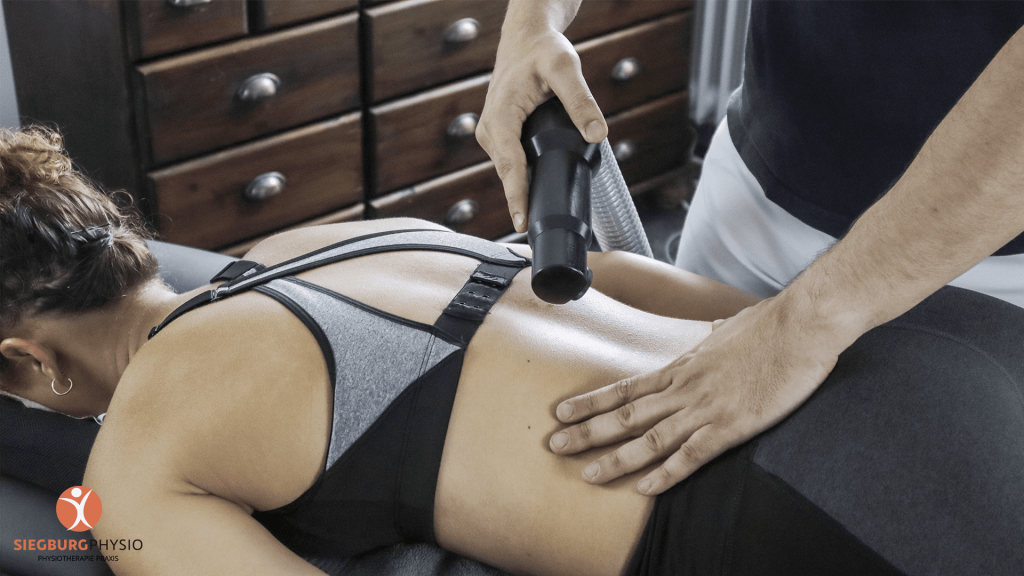 Anwendung eines Wärme- oder Kältetherapiegeräts auf dem Rücken einer Patientin in physiotherapeutischer Behandlung