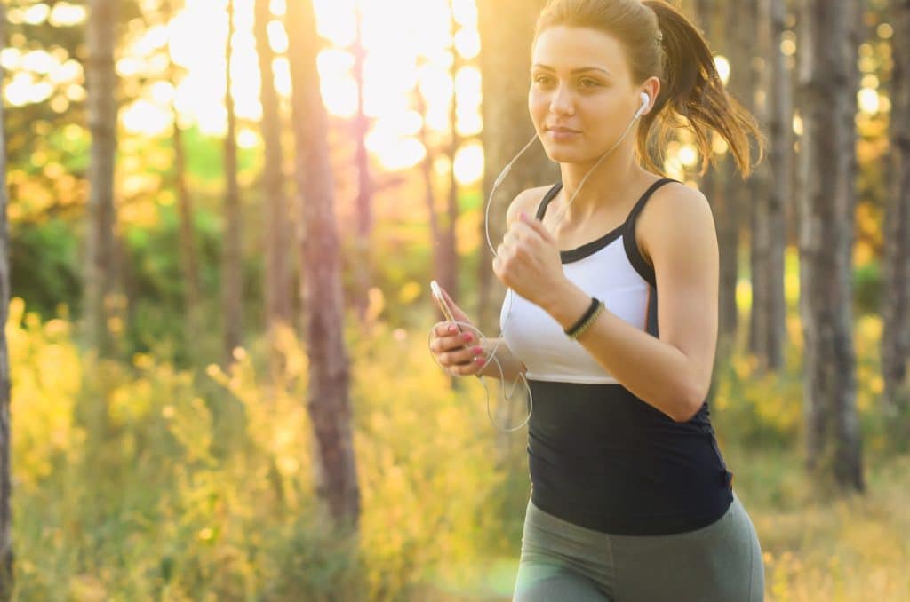 Frau joggt mit Kopfhörern durch den Wald im Sonnenlicht