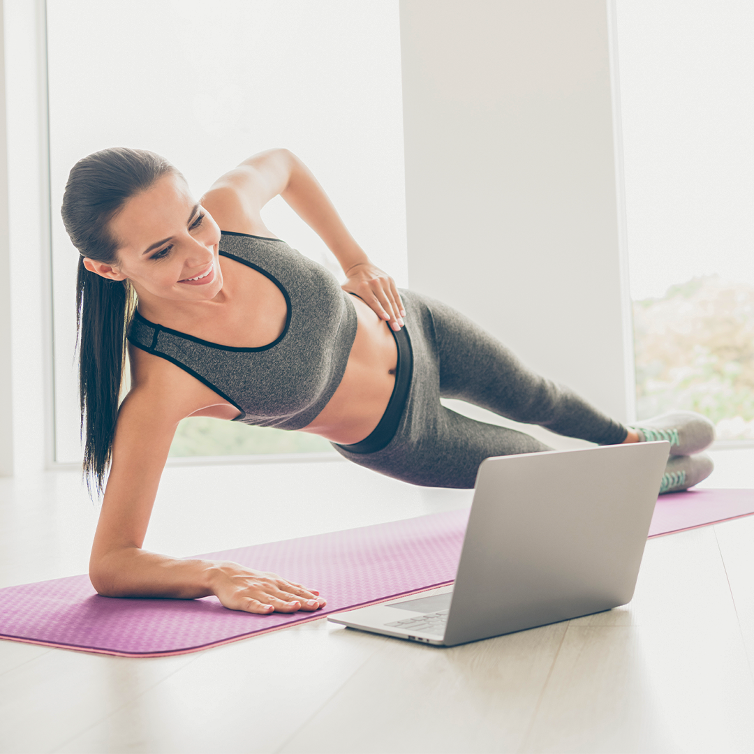 Frau beim Online-Fitnesskurs auf einer Matte mit Blick auf den Laptop