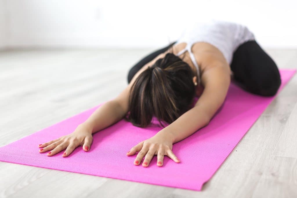 Frau macht Dehnübung in der Kindhaltung auf pinker Yogamatte