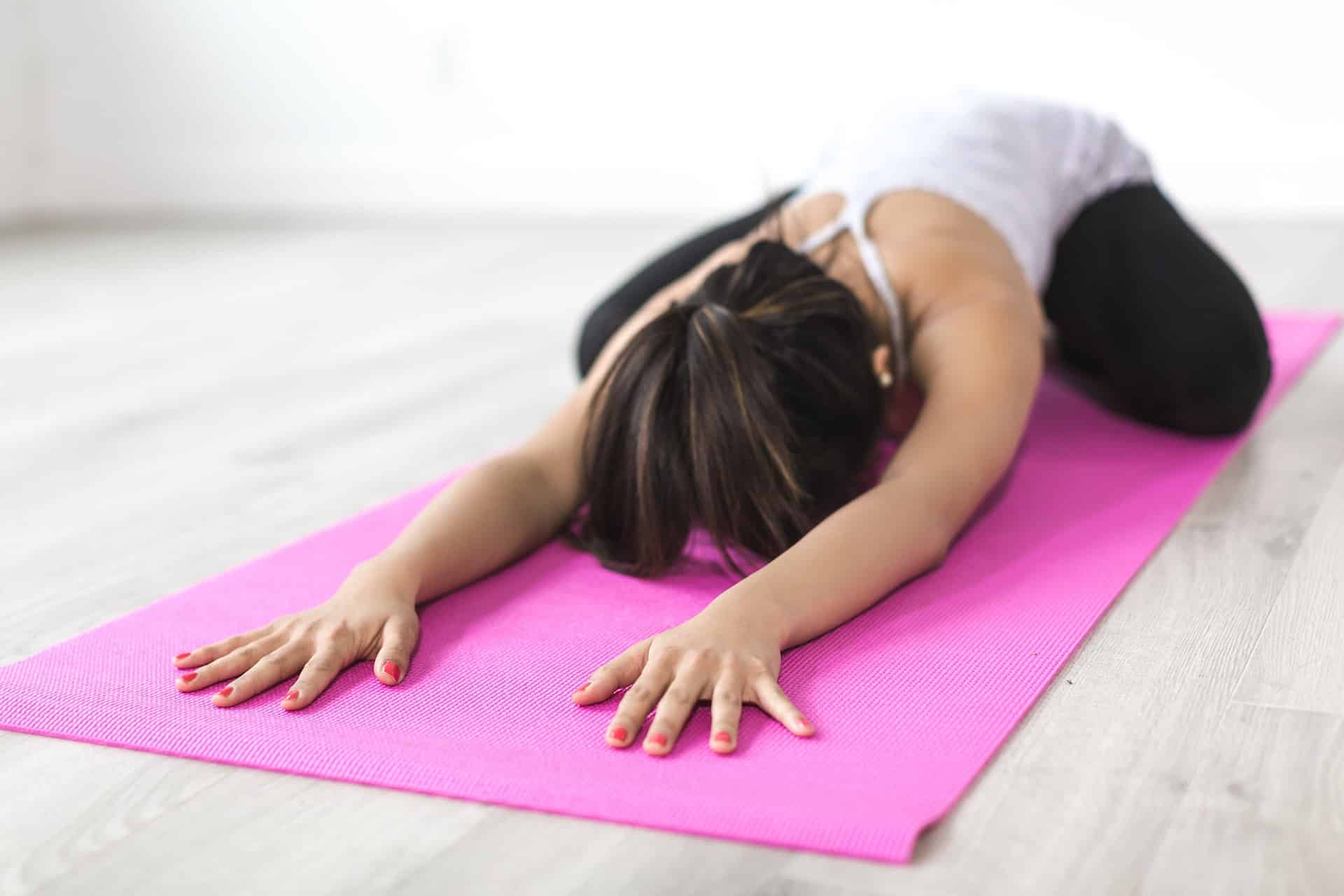 Frau macht Dehnübung in der Kindhaltung auf pinker Yogamatte